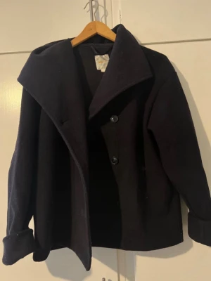 Svart ullrock med bred krage - Stilren blåa kappa i ull med bred, asymmetrisk krage och två stora knappar framtill. Rocken har uppvikta ärmslut och rak passform som ger en modern look. Perfekt för kyliga dagar när du vill vara både varm och snygg.pris kan diskuteras mer bilder eller info kom privat!!