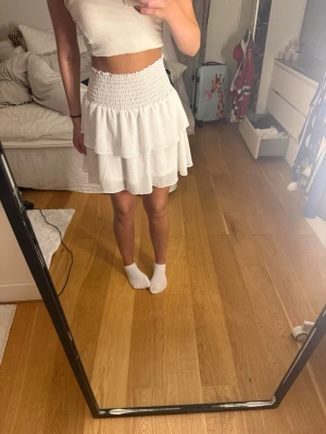 Vit volangkjol - Supersöt vit kortkjol med bred smock i midjan och dubbla volanger. Kjolen har en luftig och flowy känsla, perfekt till sommaren.  Nypris 400kr🥰