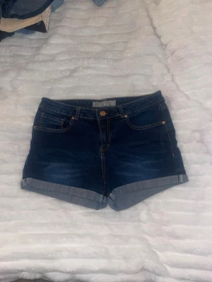 Mörkblå jeansshorts med uppvik - Snygga mörkblå jeansshorts med uppvikta benslut och klassiska fem fickor. Shortsen har kontrastsömmar och stängs med knapp och dragkedja. Perfekta till sommaren och lätta att matcha med olika toppar.