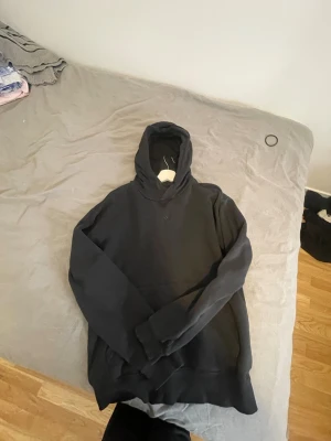 Svart hoodie från Adidas - En stilren svart hoodie från Adidas med klassisk huva och ribbade muddar. Hoodien är tillverkad i mjukt material och har en relaxed fit som passar perfekt till streetwear-looken. Diskret Adidas-logga framtill.