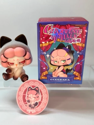 Charming Villain samlarfigur Siamese cat - Söt samlarfigur från DODORARA-serien Charming Villain. Figuren föreställer en karaktär med rosa lockigt hår, kattöron och tassar, samt röda ögon. Medföljer gör en matchande ask och en rund bricka med samma motiv. Perfekt för dig som gillar unika figurer.