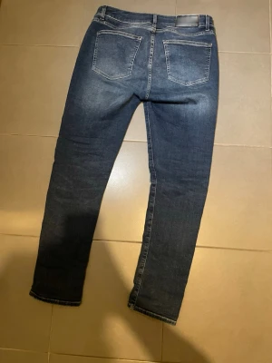 Mörkblå jeans med fina ljusa drag (slimfit) - Säljer ett par mörkblå jeans från dressman med raka ben och klassisk femficksmodell. Jeansen har dragkedjegylf och kontrastsömmar. Materialet är denim i bomullsmix och de har en stilren look utan slitningar eller dekorationer. Storlek : 31/30  Nypris:899kr