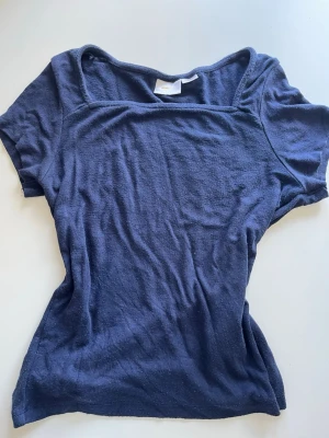 Mörkblå topp från Gina Tricot - En enkel och stilren mörkblå topp från Gina Tricot med korta ärmar och fyrkantig ringning. Tillverkad i mjukt och lätt material som känns skönt mot huden. Perfekt att matcha med jeans eller kjol för en avslappnad look.