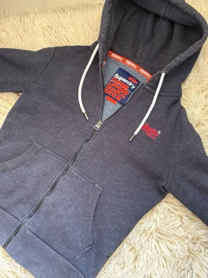Mörkgrå Superdry Zip Hoodie - En sjukt fet och unik grå kofta ifrån Superdry. Storlek - S✅ Skick - Mycket bra✅ Priset går att diskutera, kontakta för eventuella frågor och prisförslag!