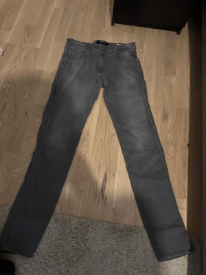 Gråa slim fit jeans från replay  - Snygga gråa slim fit jeans från replay med klassisk femficksdesign och raka ben. Jeansen har diskreta slitningar och är tillverkade i ett mjukt denimtyg som ger en skön känsla. Perfekta för dig som gillar en stilren och avslappnad look.