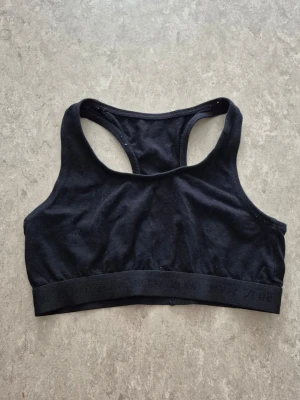 Sport-behå - En enkel och stilren svart sport-bh med brottarrygg och bred resår under bysten. Tillverkad i mjukt och stretchigt material som passar perfekt för träning eller vardagskomfort. Inga synliga loggor eller mönster.