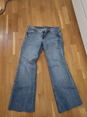Blåa utsvängda jeans - Säljer ett par klassiska blå jeans med utsvängda ben och rå kant nedtill. Jeansen har fem fickor och normal passform i midjan. Perfekta för en avslappnad och trendig look.  Jag har även klippt bort nere i benen för dem som är ungefär 165 är dem perfekt längd