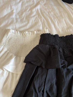 Två korta volangkjolar i svart och vitt - Säljer två söta kortkjolar med volang, en i svart och en i vitt. Båda har smock i midjan för skön passform och är gjorda i ett mjukt tyg som känns luftigt. Perfekta för varma dagar och lätta att matcha med olika toppar.💕Använda fåtal gånger så i fint skick! Pris kan diskuteras, hör av dig vid frågor!🥰