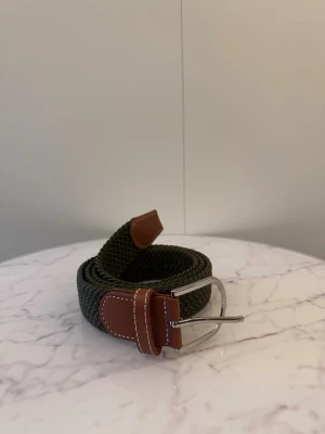 Grönt flätat bälte  - Tja säljer helt nytt klassiskt svenskt flätat bälte från Bältgallerian i storlek 110cm i längd och 3,5cm i bredd. Dem är i ett elastiskt material och finns i flera olika färger i min profil.