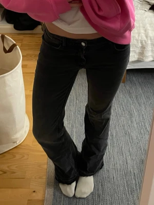 Svarta bootcut jeans med låg midja - Säljer ett par svarta bootcut jeans med låg midja och klassisk femficksdesign. Jeansen har en lätt tvättad look och är tillverkade i denim med stretch för skön passform. Perfekta för dig som gillar en avslappnad och trendig stil.