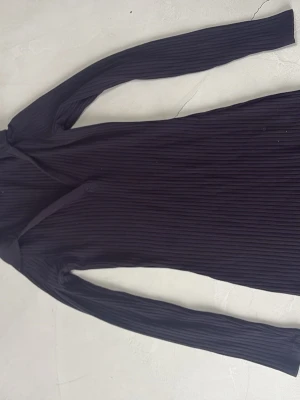 Svart ribbad långärmad klänning - En svart, ribbad klänning med lång ärm och kroppsnära passform. Klänningen är kort och har en enkel, stilren design som passar perfekt för dig som gillar minimalistiskt mode. Materialet känns mjukt och stretchigt, vilket gör den bekväm att bära. Strl egentligen S, men känns mindre skulle säga barn storlek.