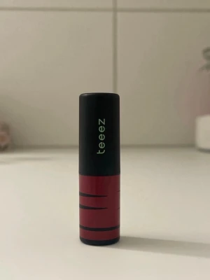 Brunt läppstift från Teeez - Snyggt läppstift från Teeez i en brun nyans. Hylsan är svart och röd med grafiskt mönster och logga på locket. Läppstiftet har en klassisk form och själva stiftet är prytt med en ingraverad logga. Perfekt för dig som gillar naturliga färger. Går att diskutera pris. 