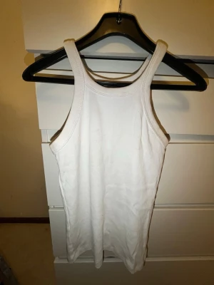 Vit ribbad linnetopp - Säljer en klassisk vit ribbad linnetopp med breda axelband och rundad halsringning. Perfekt att styla till jeans eller shorts för en enkel och fräsch look. Materialet är mjukt och stretchigt för extra komfort.