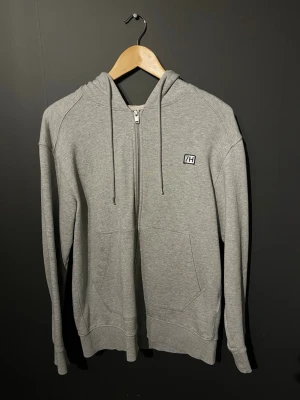 Grå zip hoodie  - Snygg grå zip hoodie från selected home med dragkedja framtill, två stora fickor och justerbar huva med snören. Liten logga på bröstet och ribbade muddar vid ärmar och nederkant. Perfekt för en avslappnad och stilren look.