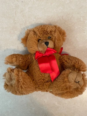 Söt brun björn gosedjur  - Björn gosedjur. Röd rosette och liten väska på ryggen,