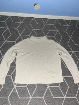 GANT sweater - Klassisk beige stickad tröja från GANT med diskret logga broderad på bröstet. Tröjan har en rak passform och är allmänt skön!