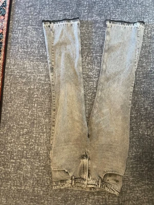 Grå tvättade raka jeans - Säljer ett par grå tvättade jeans med rak passform och klassisk femficksdesign. Jeansen har hög midja och dragkedja med knapp. Materialet är denim i bomull och färgen har en snygg vintagekänsla.