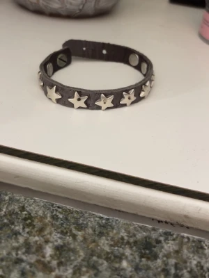Läderarmband med stjärnor  - Coolt och trendigt läderarmband med silvriga stjärnor på. Går att knäppa. Några små fläckar på vissa stjärnor men inget man tänker på. Skriv vid frågor!