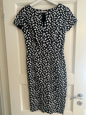 Svartvit prickig klänning från Oasis - Snygg svart klänning med vita prickar från Oasis. Modellen är figurnära med kort ärm och v-ringning framtill. Klänningen har dragkedja i ryggen och är knälång, perfekt för en trendig look. Aldrig använd pågrund av för liten storlek.