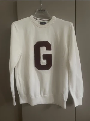 GräddVit  tröja GANT med G - Snygg vit tröja med stor mörkröd bokstav G på bröstet. Tröjan har rund halsringning, ribbade muddar och är gjord i mjukt material. Perfekt för dig som gillar enkel men sportig stil. Storlek dom på sista bilden men som S 