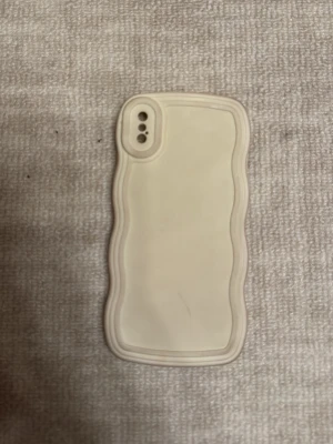 Beige vågigt mobilskal i silikon - Säljer ett beige mobilskal med vågiga kanter som ger ett unikt och trendigt utseende. Skalet är gjort i mjukt silikonmaterial och har utskärningar för kamera och knappar. Passar perfekt för dig som vill ha ett stilrent men ändå annorlunda skal till din mobil.