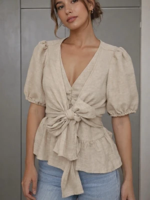 Beige omlottblus med puffärm - Säljer en beige omlottblus från Shein med puffiga korta ärmar och stor knytning framtill. Blusen har v-ringning och volangdetalj nedtill, perfekt för att skapa en trendig look. Materialet är linne och ger en skön och luftig känsla.