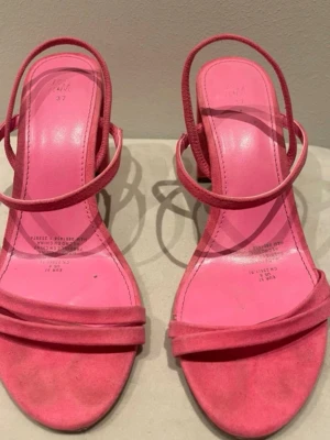 Rosa pumps med blockklack från H&M - Snygga rosa pumps från H&M med öppen tå och dubbla tunna remmar över foten. Skorna har en stabil blockklack och är tillverkade i ett mockaliknande material. Perfekta för dig som vill ha en färgklick till outfiten och gillar trendiga detaljer.