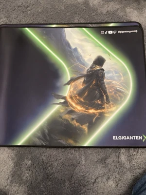 Gaming musmatta Elgiganten - Stor gaming musmatta från Elgiganten med tryck av en fantasy-inspirerad karaktär och neon-gröna detaljer. Ovansidan har en slät textilyta med tryck, undersidan är svart och halkfri. Perfekt för gaming-setupen och ger bra precision till musen.