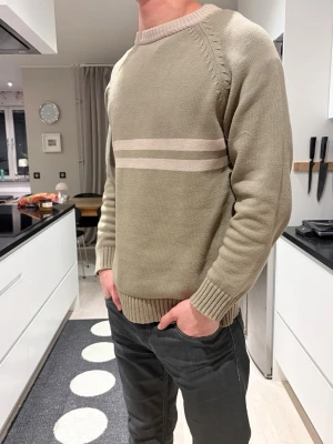 Mintgrön stickad tröja med ränder - Snygg beige stickad tröja med två ljusa horisontella ränder över bröstet. Tröjan har rund halsringning, raglanärmar och ribbade muddar vid ärmslut och nederkant. Perfekt för dig som gillar en enkel men stilren look.