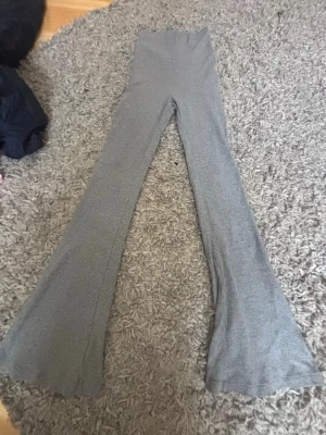 Grå ribbade mjukisbyxor med utsvängda ben - Säljer ett par grå mjukisbyxor med ribbad struktur och utsvängda ben. Byxorna har hög midja med bred linning och är gjorda i ett mjukt, stretchigt material som sitter skönt. Perfekta för en avslappnad och trendig look.