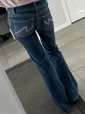 Blå bootcut jeans från Nelly - Snygga blå bootcut jeans från Nelly med klassisk femficksdesign och coola vita zigzag-sömmar på bakfickorna. Jeansen har normal midja och är tillverkade i denim med stretch för skön passform. Perfekta för dig som gillar retrostil och bekväma jeans.