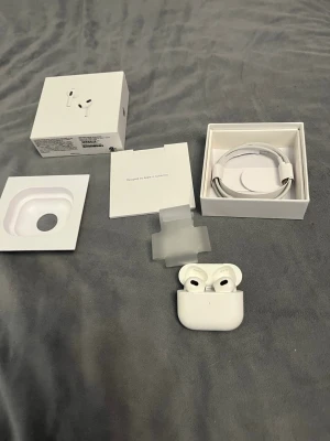 Apple AirPods gen 3 med laddningsetui 1;1 - Säljer ett par vita Apple AirPods Pro med tillhörande laddningsetui och originalförpackning. Hörlurarna är trådlösa och har en stilren, kompakt design i blankt plastmaterial. Medföljer även laddningskabel och dokumentation. 1:1 