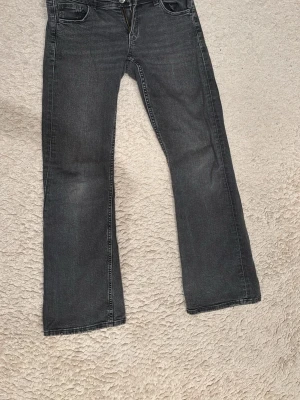 Svarta bootcut jeans - Säljer ett par svarta bootcut jeans med klassisk femficksdesign och knappgylf. Jeansen har en lätt tvättad look och raka ben. Perfekta för en avslappnad och trendig stil.