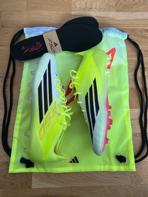 Adidas F50 fotbollsskor gul/svart - Säljer ett par Adidas F50 fotbollsskor i neon-gult med svarta detaljer och röda inslag. Skorna har en smal och aerodynamisk form, tillverkade i syntetmaterial för lätt vikt och bra grepp. Medföljer original skopåse och extra innersulor.