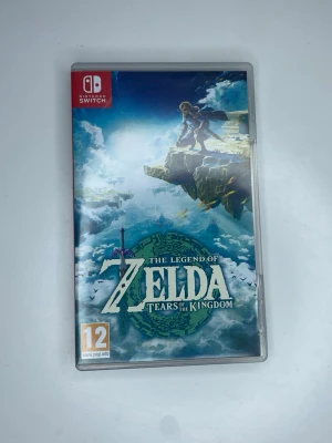 The Legend of Zelda: Tears of the Kingdom - Nintendo Switch-spelet The Legend of Zelda: Tears of the Kingdom kommer i ett plastfodral med färgstark omslagsbild. Spelet är ett actionäventyr i en öppen värld med episka miljöer och ikonisk fantasykänsla. Omslaget har blå, gröna och vita toner.