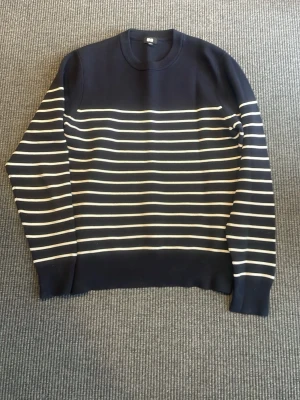 Marinblå randig tröja Uniqlo - Säljer en marinblå stickad tröja från Uniqlo med vita horisontella ränder över bröstet och ärmarna. Tröjan har rund halsringning och ribbade muddar. Perfekt för dig som gillar klassisk och stilren design. Fler frågor eller funderingar hör av er i Dm!