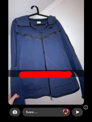 Blå zip hoodie från Nike - Mörkblå hoodie från Nike med dragkedja framtill och svarta detaljer över bröstet. Klassisk huva och två fickor på sidorna. Perfekt för en sportig och avslappnad stil. Tillverkad i mjukt material för extra komfort.