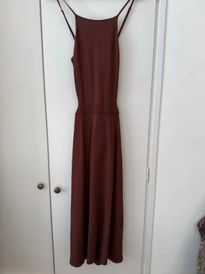 Brun klänning Other Stories med smala band urigning bak  - Snygg brun  klänning med smala axelband och markerad midja. Klänningen har en rak överdel och ett lätt utställt kjolparti som ger en avslappnad men stilren siluett. Perfekt för dig som gillar minimalistisk och trendig stil.urigning bak. Strl XS 
