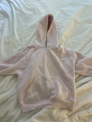 Ljusrosa hoodie med magficka - En stilren ljusrosa hoodie från Ginatricot med klassisk huva och stor magficka framtill. Hoodien har ribbade muddar vid ärmslut och nederkant. Perfekt för en avslappnad och trendig look. Materialet känns mjukt och bekvämt, troligen bomullsblandning.