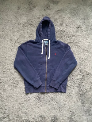 Marinblå hoodie från Polo Ralph Lauren - Snygg marinblå hoodie från Polo Ralph Lauren med dragkedja,  och den klassiska röda loggan broderad på bröstet. 