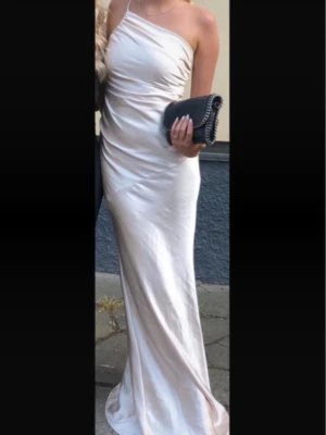 Champagnefärgad långklänning oneshoulder - Elegant långklänning i champagnefärgat tyg med oneshoulder-design och figurnära passform. Klänningen har en mjuk glans och faller snyggt längs kroppen, perfekt för bal. Väldigt lång i modellen så passar till och med 1,75-1,80cm Skriv vid frågor💕🙌🏼