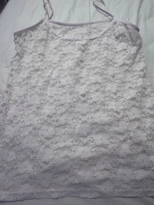 Vit spetslinnetopp med smala band - Säljer en söt vit linnetopp med tunna axelband och blommig spets över hela plagget. Toppen har rundad halsringning och är perfekt för dig som gillar romantisk och feminin stil. Passar att styla med jeans eller kjol för en fräsch look.