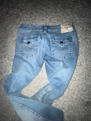 Ljusblå True Religion jeans - Säljer ett par ljusblå jeans från True Religion med klassiska kontrastsömmar och snygga fickdetaljer bak. Jeansen har raka ben och femficksmodell. Materialet är denim i bomull med en skön tvättad look. Perfekta för en avslappnad och trendig stil.