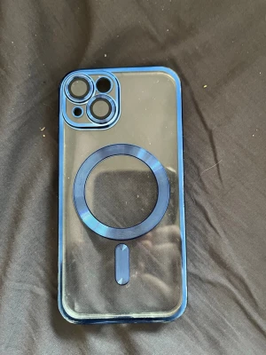 Blått MagSafe-kompatibelt mobilskal - Snyggt mobilskal med blå ram och transparent baksida, designat för iPhone 13 med MagSafe-kompatibilitet. Skalet har markerade kamerahål och en rund MagSafe-ring i blått. Tillverkat i tålig plast som skyddar mobilen utan att dölja dess design.