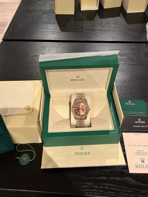 Datejust silver och roséguld - Säljer en exklusiv Datejust med silver och roséguld länk. Urtavlan är brun med datumvisning och markerade index. Klockan har en räfflad bezel i roséguld och kommer i originalbox med certifikat och tillbehör. Perfekt för dig som vill ha något riktigt stilrent och lyxigt.