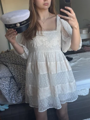 Vit kort klänning - studentklänning  - Superfin vit kort klänning med puffärmar, fyrkantig ringning och broderade blommor på bröstet. Klänningen har prickigt mönster i tyget och volangdetaljer. Helt nytt skick 