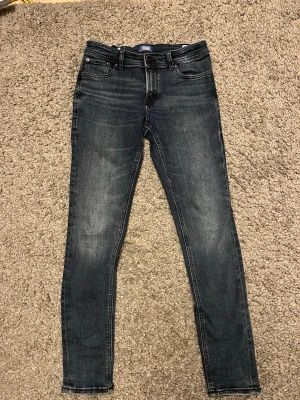 Mörkgrå skinny jeans Jack & Jones - Snygga mörkgrå skinny jeans från Jack & Jones med klassisk femficksdesign och diskreta slitningar. Jeansen har en smal passform och är tillverkade i stretchigt denim för extra komfort. Perfekta för en trendig och avslappnad stil.