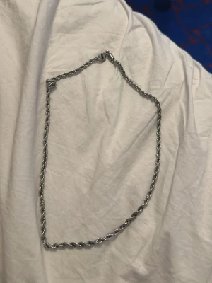 Silverfärgat tvinnat halsband - Snyggt halsband i silverfärg med tvinnad kedja som ger en cool och modern look. Passar perfekt till streetwear eller för att lyfta en enkel outfit. Halsbandet har ett klassiskt lås och är gjort av rostfritt stål, som aldrig tappar sin färg. Längden på halsbandet är 50 cm.