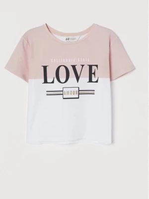 Rosa och vit t-shirt från H&M - T-shirt från H&M i tvåfärgad design med ljusrosa upptill och vit nedtill. Tryck framtill med texten 'LOVE' och 'AMOUR' i svart och guld. Klassisk rund halsringning och korta ärmar. Perfekt för en avslappnad och trendig look.