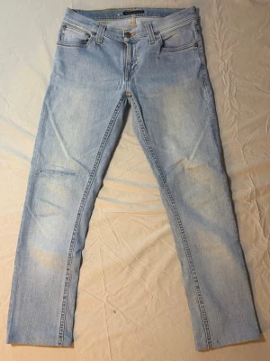 Nudie jeans ljusblå – Slim fit – 28/34 – Mycket bra skick - Nudie jeans ljusblå – Slim fit – 28/34 – Mycket bra skick  Säljer ett par ljusblå Nudie jeans, slim fit, storlek 28/34, i mycket bra skick. Riktigt snygg ljus tvätt som ger en fräsch och clean look – perfekt för vår, sommar och ljusare outfits.  Slim passform som sitter snyggt utan att bli för tight. Funkar lika bra till sneakers som loafers för en mer uppklädd stil.  Mått: Midja: 36 cm Längd: 89 cm  • Märke: Nudie Jeans • Passform: Slim • Färg: Ljusblå • Skick: Mycket bra  Nudie 4